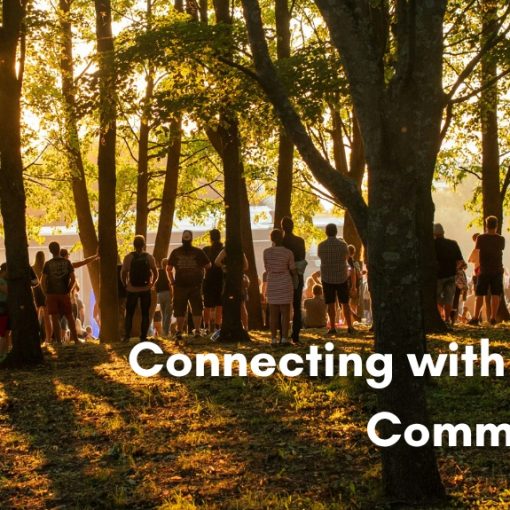 A large group of people gathered together in a sunlit forest during golden hour, with the text "Connecting with Your Community" overlaid in bold white lettering on the bottom right.