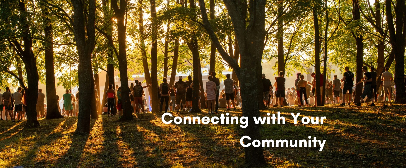 A large group of people gathered together in a sunlit forest during golden hour, with the text "Connecting with Your Community" overlaid in bold white lettering on the bottom right.