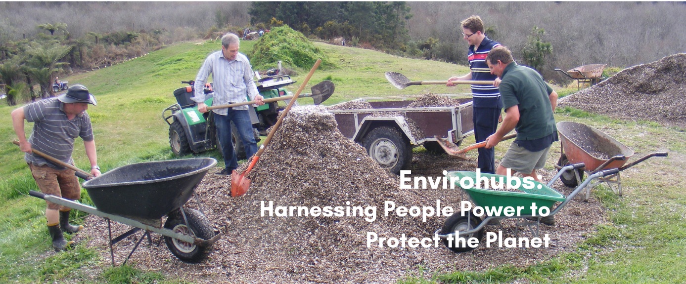 Four volunteers shoveling mulch from a trailer and gravel pile into wheelbarrows during an Envirohubs community planting event